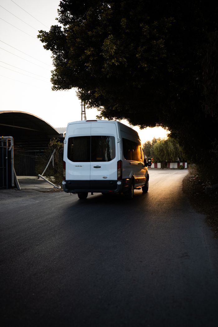 A white minivan drives on a quiet road under trees during a serene sunset.